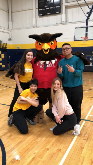 Four students posing in gymnasium with Swoop mascot